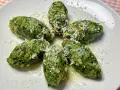 Strangolapreti alla trentina, verdi e saporiti, spolverati di formaggio grattugiato su un piatto bianco.