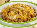 Piatto di gramigna alla salsiccia, condita con ragù e parmigiano grattugiato, servita in una ciotola con bordo verde.