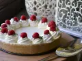 Cheesecake senza gelatina decorata con panna montata e lamponi freschi, pronta per essere servita.