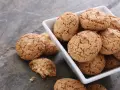 Un mucchio di croccanti biscotti alle mandorle in una ciotola bianca, alcuni sparsi su una superficie grigia.