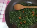 Cicoria in padella con peperoncino, un contorno saporito e salutare. Un cucchiaio di legno mescola le foglie verdi.