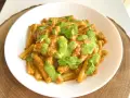 Un piatto di pasta alla Portofino, con un sugo rosso e un pesto verde brillante, guarnito con foglie di basilico fresco.