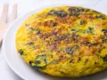 Frittata di spinaci dorata e invitante su un piatto bianco, con un utensile in legno sullo sfondo.