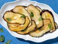 Fette di melanzane grigliate, guarnite con menta fresca e aglio, un contorno di verdure saporito.