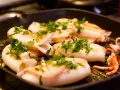 Seppie alla griglia succulente, cosparse di prezzemolo fresco, cuociono in una padella scanalata, pronte per essere gustate.