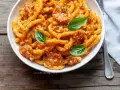 Busiate alla trapanese, un piatto di pasta siciliana con un ricco sugo rosso, guarnito con basilico fresco.