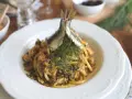 Un piatto di pasta con le sarde, guarnito con finocchietto fresco e due pesciolini interi. Un classico siciliano pronto da gustare.
