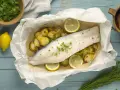 Ombrina al forno con patate e limone, guarnita con erba cipollina fresca. Un piatto leggero e saporito.