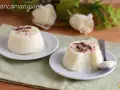Biancomangiare ricetta originale siciliana: due dolci al cucchiaio bianchi, guarniti con codette colorate e scaglie di cioccolato, su piattini bianchi.