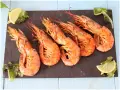 Cinque succulenti gamberoni alla griglia, serviti su una pietra scura con spicchi di limone e insalata fresca.
