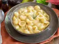 Una ciotola di minestra di patate cremosa con pasta a conchiglia, guarnita con rosmarino. Un piatto confortante e saporito.