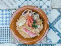 Un invitante cous cous di pesce con gamberi, calamari, cozze e pesce rosso, guarnito con prezzemolo, servito in una ciotola di terracotta su un piatto di maioliche.