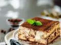 Una fetta di tiramisù ricetta originale, cosparso di cacao e decorato con menta fresca.