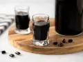 Due bicchierini e una bottiglia di liquore alla liquirizia scuro, con caramelle di liquirizia sparse su un tagliere di legno.
