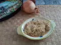 Ciotola con cipolle in agrodolce, accanto una cipolla intera e un piatto decorato.