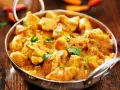 Bocconcini di pollo al curry, un piatto speziato e profumato, servito in una ciotola metallica su un tavolo di legno.