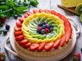Una colorata crostata di frutta, con fragole, kiwi, ananas e frutti di bosco, su un tavolo di legno rustico.