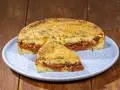 Pitta di patate ripiena di sugo, olive e cipolle, con una crosta dorata di pangrattato.
