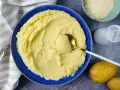 Un piatto invitante di puro di patate cremoso, pronto per essere gustato. Accanto, patate fresche, sale e formaggio grattugiato.