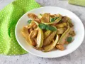 Zucchine in agrodolce, un piatto colorato e saporito, guarnito con basilico fresco su un piatto bianco, accanto a un tovagliolo a pois verdi.