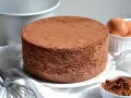 Un soffice pan di spagna al cacao, pronto per essere farcito. Accanto, uova fresche e cacao in polvere.