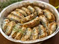 Sardine al forno dorate e croccanti, disposte in una teglia d'alluminio con rametti di rosmarino.