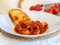Un piatto invitante di moscardini in umido, con tentacoli succulenti in salsa rossa, accompagnati da una fetta di pane tostato dorato.
