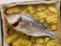 Orata al forno dorata e succulenta, adagiata su un letto di patate croccanti e aromatiche.