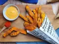 Patate dolci al forno croccanti, servite in un cono di carta con una salsa cremosa e paprika.