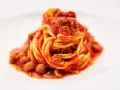 Un piatto di spaghetti alla teramana, conditi con un ricco sugo di pomodoro e polpettine, serviti su un piatto bianco.