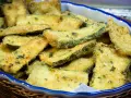 Fette di zucchine gratinate in padella, dorate e croccanti, servite in una ciotola blu bordata di bianco.