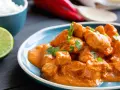 Spezzatino di pollo cremoso e speziato, guarnito con prezzemolo fresco, servito su un piatto blu con riso bianco e spicchio di lime.