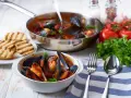 Cozze alla tarantina fumanti in una ciotola bianca, accompagnate da pane grigliato e ingredienti freschi.