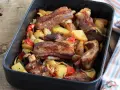 Succulente costine al forno con patate, peperoni e cipolle in una teglia.