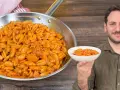 Un uomo sorride mostrando una ciotola di gnocchetti alla campidanese, accanto a una padella piena dello stesso piatto.