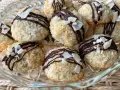 Deliziosi dolcetti al cocco, ricoperti da cioccolato fondente e scaglie di cocco croccante, su un piatto di vetro.