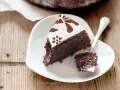 Una fetta di torta caprese ricetta originale napoletana, cosparsa di zucchero a velo e cacao, su un piattino bianco a forma di cuore.