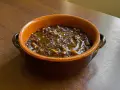 Un gustoso piatto di pasta e lenticchie, condito con olio d'oliva, servito in una ciotola di terracotta su un tavolo di legno.