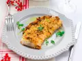 Delizioso merluzzo impanato al forno, dorato e croccante, guarnito con erbe fresche e servito su un piatto grigio.