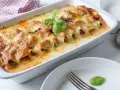 Cannelloni ripieni di carne macinata e mozzarella, cotti al forno e gratinati, con una foglia di basilico fresco.