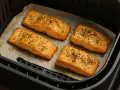 Quattro filetti di salmone in friggitrice ad aria, dorati e conditi con erbe aromatiche, pronti per essere gustati.