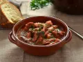 Un saporito polpo alla pignata, cotto lentamente in umido, servito in una ciotola di terracotta con pane fresco a lato.