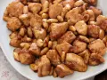Close-up of bite-sized chicken pieces and almonds coated in a glossy brown sauce on a white plate.