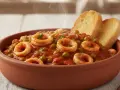 Un gustoso piatto di seppie con piselli in umido, servito in una ciotola di terracotta con crostini di pane.