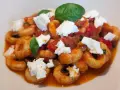 Anellini alla pecorara con pomodoro, zucchine e ricotta fresca, guarniti con foglie di basilico.