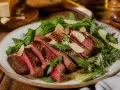 Tagliata di manzo succulenta, affettata e servita su un letto di rucola fresca, guarnita con scaglie di parmigiano.