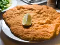 Una cotoletta dorata, grande come un'orecchia di elefante, servita con una fetta di limone e un'insalata fresca.