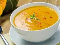 Una cremosa vellutata di zucca, guarnita con rosmarino e paprika, pronta per essere gustata.
