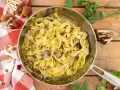 Tagliatelle ai funghi cremose in padella, con funghi freschi e prezzemolo su fondo di legno.