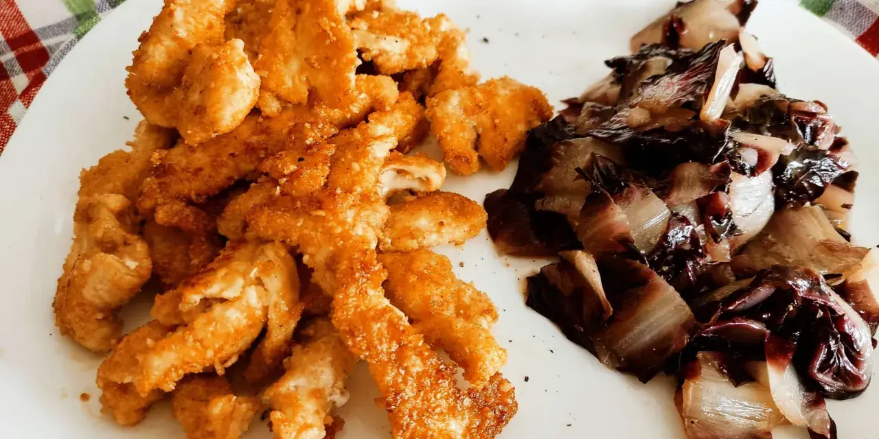 Straccetti di pollo al forno dorati e croccanti, serviti con radicchio stufato. Un piatto semplice e gustoso.